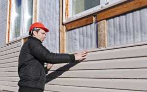 A worker installs panels beige siding on the facade of the house